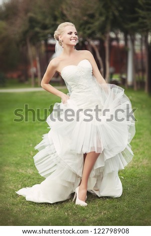 wedding: playful beautiful bride dancing in white wedding dress hairstyle and bright makeup and waiting for groom. alluring blond woman in love posing in bridal dress outdoor smiling and looking happy