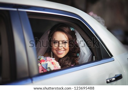 happy beautiful bride in car with bridal bouquet hairstyle and bright makeup at wedding day. woman in white dress at wedding day waiting for groom and posing. Concept of happiness and love. Newlywed