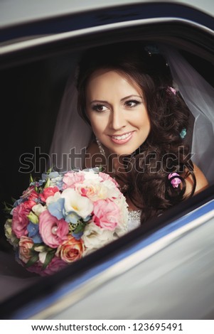 happy beautiful bride in car with bridal bouquet hairstyle and bright makeup at wedding day. woman in white dress at wedding day waiting for groom and posing. Concept of happiness and love. Newlywed