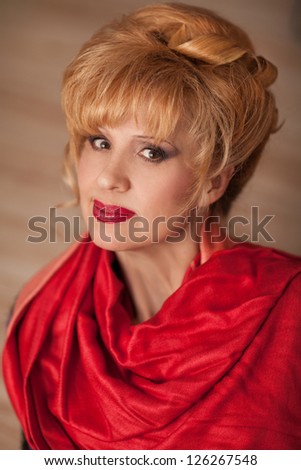 elegant middle aged woman with bright makeup and fashion hairstyle in red scarf posing at home. Rich happy blond stylish businesswoman relaxing and smiling in evening. cheerful middle aged woman