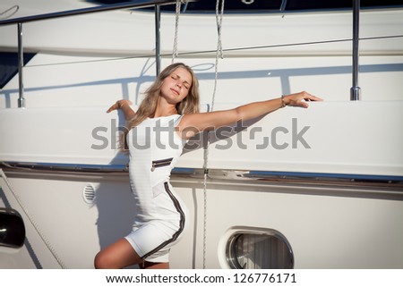 Beautiful blonde woman near yacht enjoy moment of happiness at vacation on sea. Playful alluring sexy girl posing at summer day in bay. gorgeous lady in white dress having fun. Fashion model at yacht