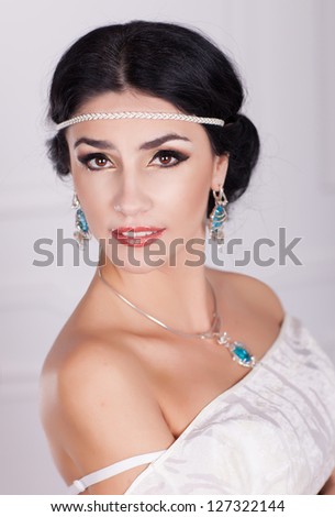 Woman in white dress - bride with bright makeup and fashion greek hairstyle in wedding dress and jewelry waiting for groom at home. stylish girl in vintage dress have final preparation for wedding