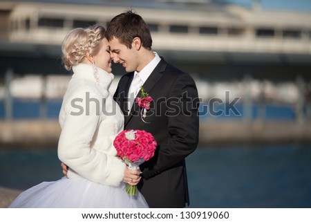 Bride and groom embrace each other and laughing on their winter wedding day near sea enjoying happiness and love. Happy Newlywed holding hands while facing each other and lovely smiling. roses bouquet