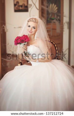 Gorgeous bride blonde with wedding bouquet makeup and hairstyle in bridal dress diamond jewelry at home waiting for groom. Jewelry and beauty. Rich happy girl  have final preparation for wedding