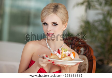 Beautiful sexy blonde woman in restaurant cafe with ice cream tiramisu cake alluring girl in red dress hairstyle and makeup eating dessert. Beauty fashion slim model rich retro lady in vintage dress