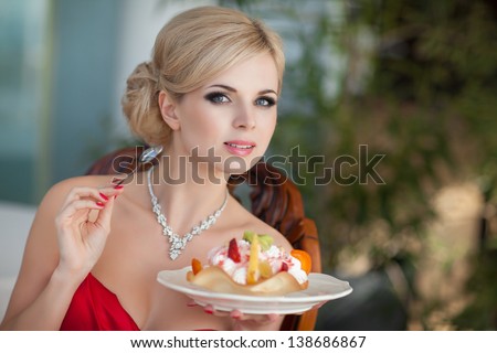 Beautiful sexy blonde woman in restaurant cafe with ice cream tiramisu cake alluring girl in red dress hairstyle and makeup eating dessert. Beauty fashion slim model rich retro lady in vintage dress