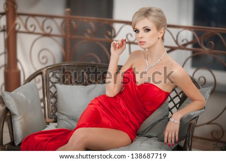 Beautiful blonde sexy woman in red dress beauty jewelry model slim girl with makeup  hairstyle smiling and looking happy posing. Alluring Sexy blond woman fashion rich lady in cafe restaurant in hotel