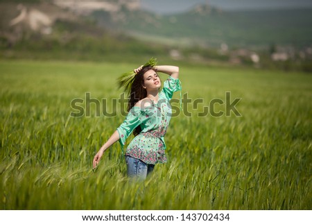 Beautiful happy woman girl smiling outdoors on green wheat field in summer nature. Pretty woman with natural makeup curly hairstyle in country village with green wheat. Attractive beauty girl in park