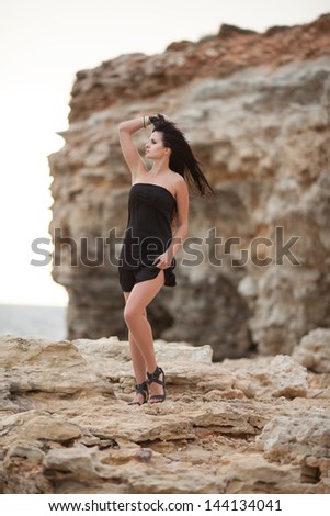 Beautiful woman at sea beach on ocean rocks relaxing happy brunette girl outdoors at vacation. Sexy fashion woman on beach. Summer beach vacation holidays. Romantic woman on beach.  travel getaway