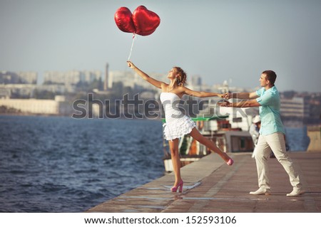 Teenage couple embracing on dating with bunch of balloons hearts. Beautiful Young Couple man and woman in love. Smiling man and woman hugging. happy loving couple. Young couple in love outdoor.