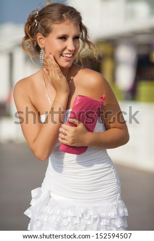 beautiful surprise woman walking outdoors. Happy smiling teenager girl at vacftion outdoors. Trendy fashion woman in white dress at street. Woman with modern pink bag clutch. Teen girl on dating