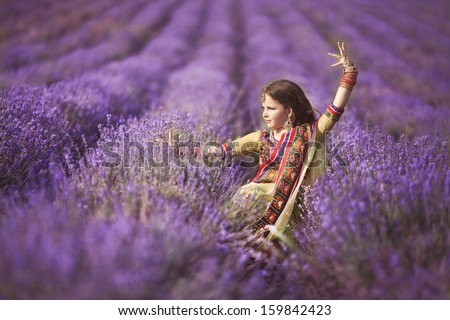 Beautiful Little Indian Girl Outdoors In Lavender Field, Aromatherapy. Adorable Baby Girl Dancing At Lavender Flowers. Happy Indian Kid In Traditional Sari. Cute Girl Bellydancer.