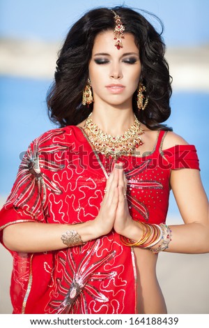Beautiful Indian Woman in Traditional red dress and golden jewelry outdoors. Portrait of young pretty Indian girl. Native Indian lady praying.
