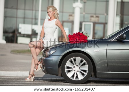 Happy woman in luxury car with roses flowers at Valentine\'s day. Sexy woman with bouquet in car. Beautiful rich woman smiling portrait. Sensual young girl with car. soft light shot.
