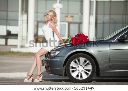 Happy woman in luxury car with roses flowers at Valentine's day. Sexy woman with bouquet in car. Beautiful rich woman smiling portrait. Sensual young girl with car. soft light shot.