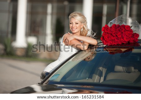 Happy woman in luxury car with roses flowers at Valentine\'s day. Sexy woman with bouquet in car. Beautiful rich woman smiling portrait. Sensual young girl with car.