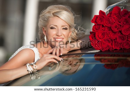 Happy woman in luxury car with roses flowers at Valentine\'s day. Sexy woman with bouquet in car. Beautiful rich woman smiling portrait. Sensual young girl with car.