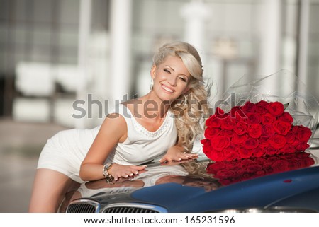 Happy woman in luxury car with roses flowers at Valentine's day. Sexy woman with bouquet in car. Beautiful rich woman smiling portrait. Sensual young girl with car.