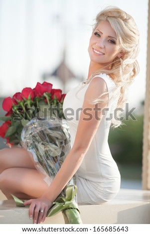 Beautiful happy woman with roses flowers outdoor. Sexy blond woman with rose bouquet in park. Valentines Day.