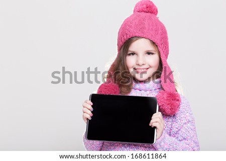 Cute winter little girl with laptop tablet pc, adorably baby girl in woolen accessories at studio. Happy little girl with computer. Space and white background.