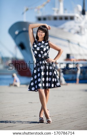 Beautiful Young Woman Outdoors near sea and cruise ship. Vacation summer woman walking outdoor. Sexy brunette woman posing near sea.