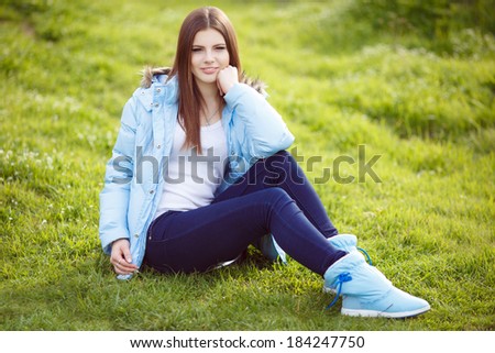 Beautiful young girl in green spring park lifestyle portrait. Smiling teenager girl relaxing on nature at spring time. Teen female enjoying life. Series.