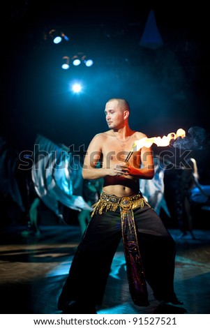 The young sexual fakir man fire eater actor   eating fire dangerous fiery fascinating performance in circus at night  and breathing fire with sexy  young bellydancers