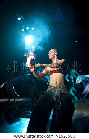 The young sexual fakir man fire eater actor   eating fire dangerous fiery fascinating performance in circus at night  and breathing fire and beautiful sexy bellydancers with shawl