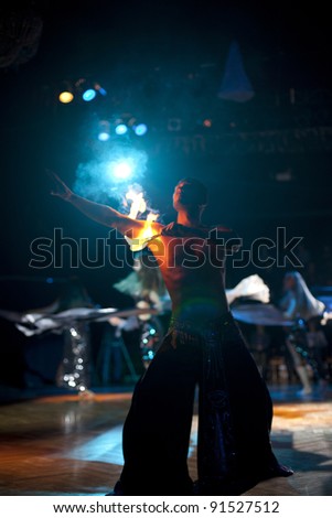 The young sexual fakir man fire eater actor  eating fire dangerous fiery fascinating performance in circus at night  and breathing fire blowing fire from his mouth and the belledancers with shawl