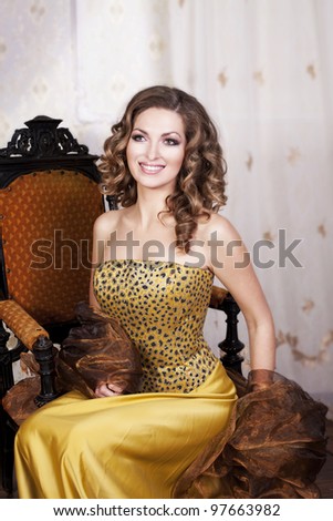 beautiful rich romantic woman in golden dress sitting and smile in luxurious vintage-style retro interior with blond healthy glossy hair. Evening - night. Fashion style shot