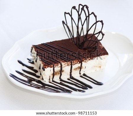 Slice of tasty chocolate tiramisu cake traditional Italian biscuit dessert on white plate on table in restaurant. Piece of unhealthy calories fat food .