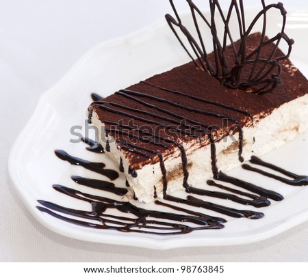 Slice of tasty chocolate tiramisu cake traditional Italian biscuit dessert on white plate on table in restaurant. Piece of unhealthy calories fat food .