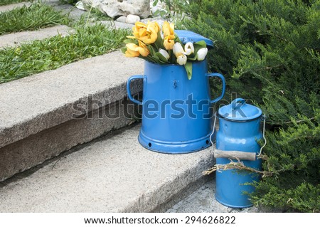 Blue retro metal enamel jugs on old stone steps in back yard house garden