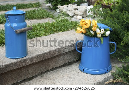 Blue retro metal enamel jugs on old stone steps in back yard house garden