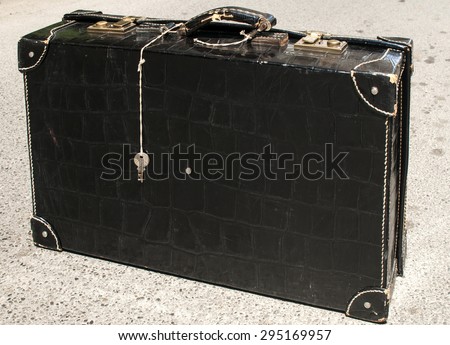 Retro vintage used suitcase of black patent leather on asphalt surface