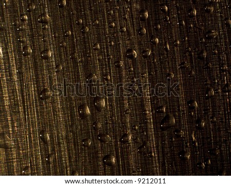 Water drops on a metal surface. The metal structure at light consists of points of different colors. Macro.