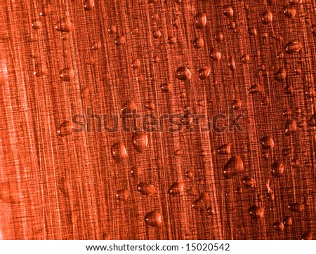Water drops on a red metal surface. The metal structure at light consists of points of different colors. Macro.