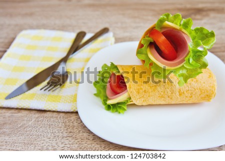 Wrapped tortilla sandwich rolls with lettuce, cheese, tomatoes and ham on a white plate