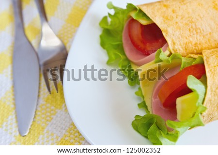 Wrapped tortilla sandwich rolls with lettuce, cheese, tomatoes and ham closeup