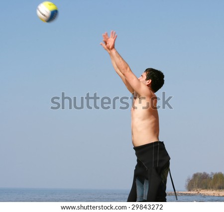 young guy (kite surfer) playing volley-ball on the beach