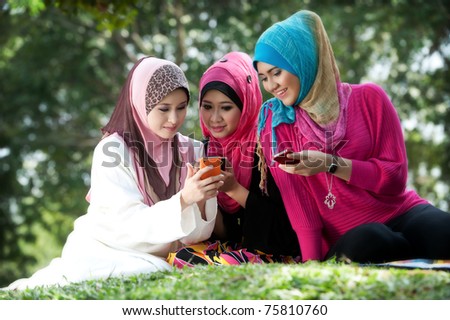 young muslim woman in head scarf meet friends and using phone in the park