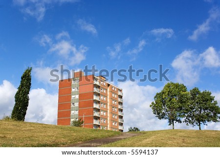 block of flats and trees,on top of grassy hill with blue sky and white cloud background