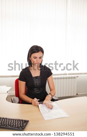 Young woman in a black dress is sitting at a desk in the office
