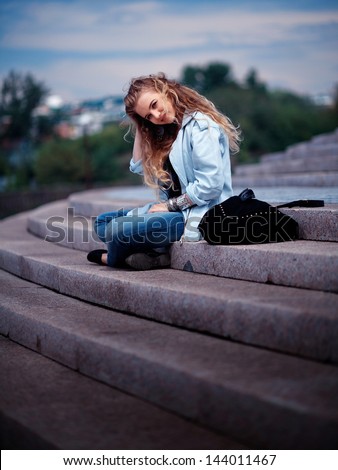 Attractive young blond woman sat on steps outdoors.
