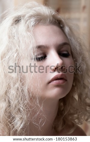 Half body portrait of topless young woman with long curly blond hair covering breasts with hands.