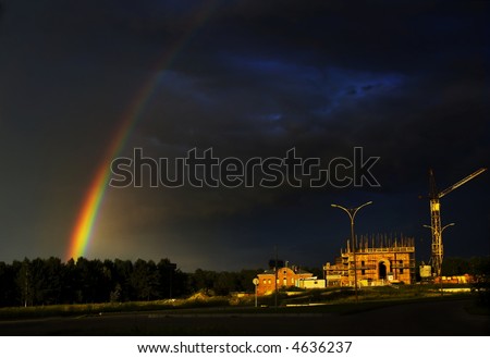 Bright rainbow on a background of the dark clouds, the frozen construction of a temple