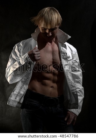 Muscular male bodybuilder young man in a white jacket on a naked torso  in studio with a black background