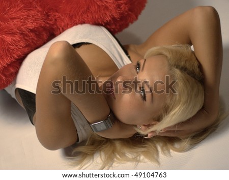 Half body portrait of blond haired young woman with bare chest hugging fluffy cushion or pillow