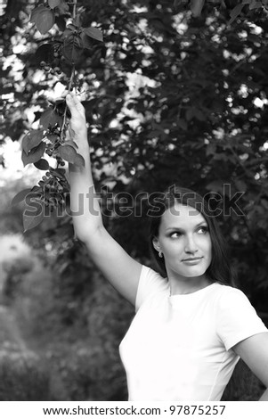 The long-haired girl in a white vest with the lifted hand against foliage