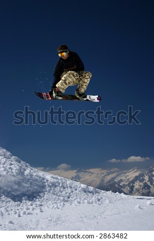 Snowboarder in moro desert pants jumping high - winter mountain action scene
